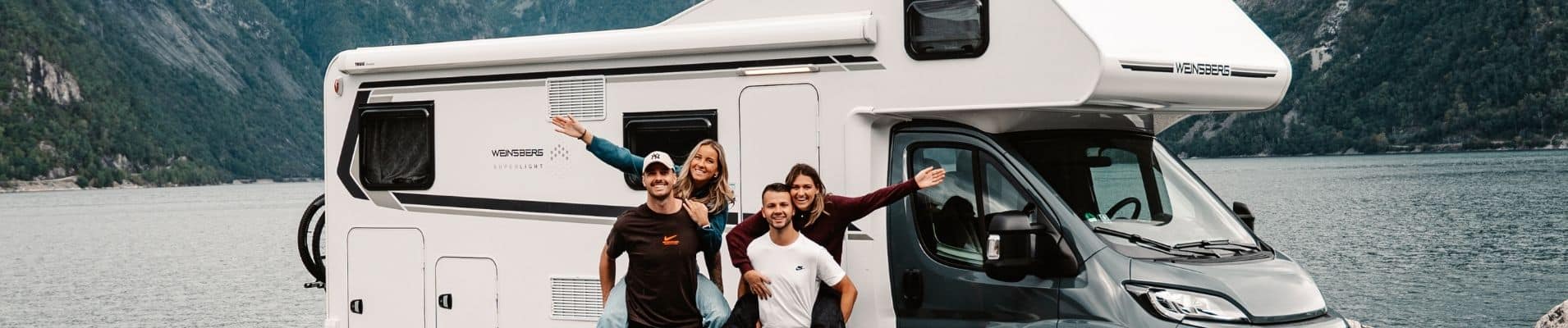 Freunde im Wohnmobilurlaub am Tisch neben ihrem gemieteten Wohnmobil